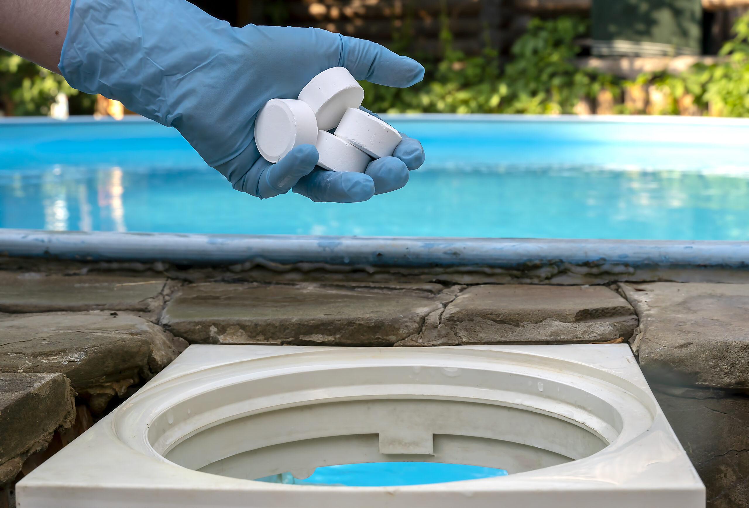 Female hand puts white tablets into pool skimmer. Cleaning, disinfection of water in the swimming pool.