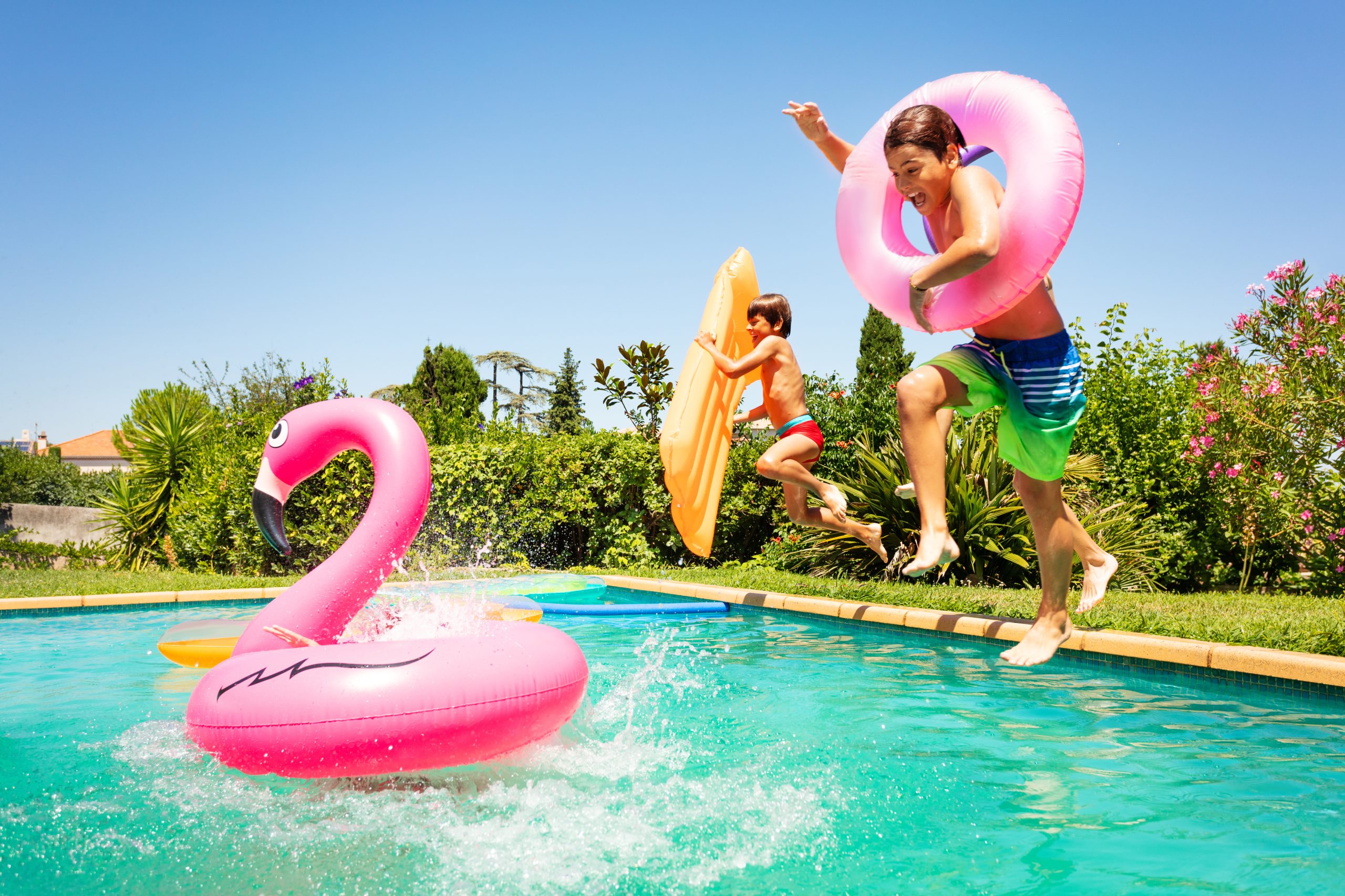 Portrait of age-diverse boys and girls, happy friends, jumping in water with inflatable swim floats, enjoying pool party in summer
